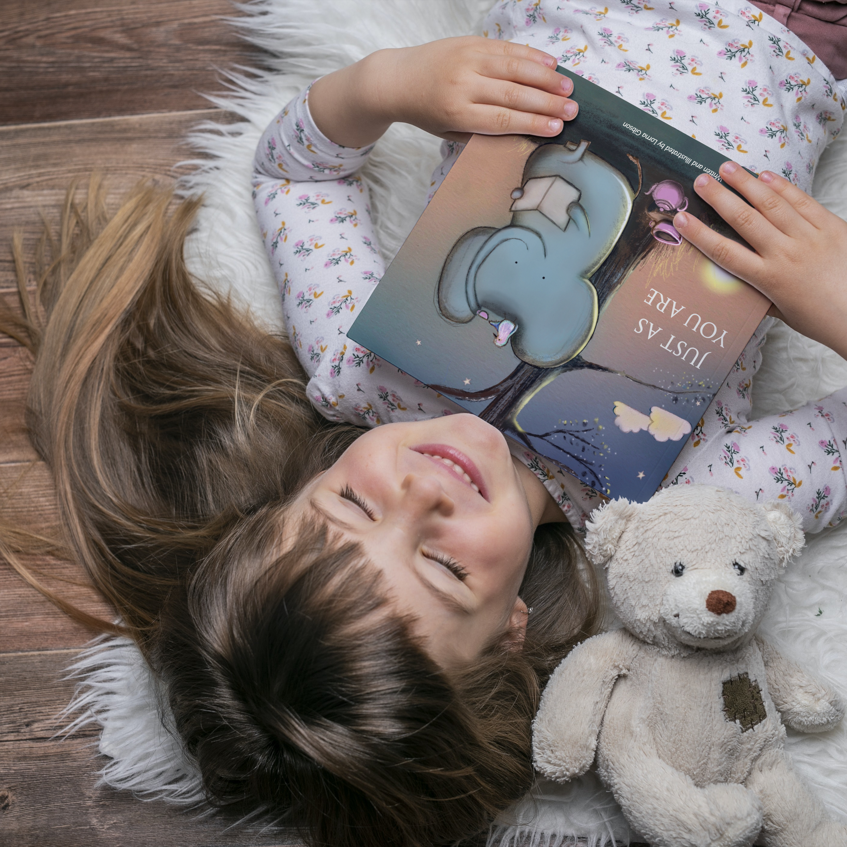 Gift ideas for kids - Image shows a little girl holding a copy of Just As You Are beside her teddy bear lying on a cosy fluffy rug